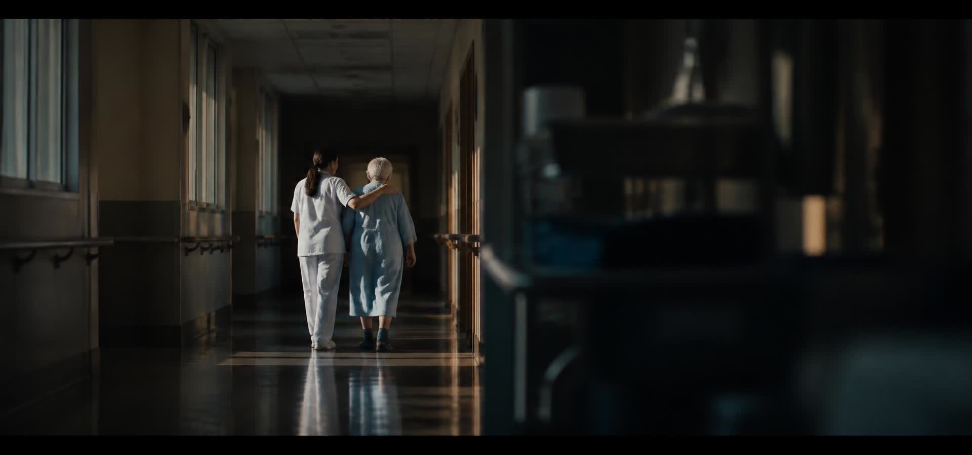 A nurse walking a patient down a sunlit hospital corridor
